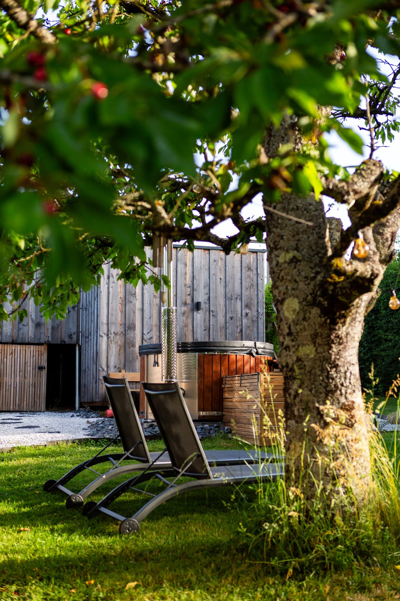Transats et fauteuils de détente sur la terrasse du gîte au cœur du verger